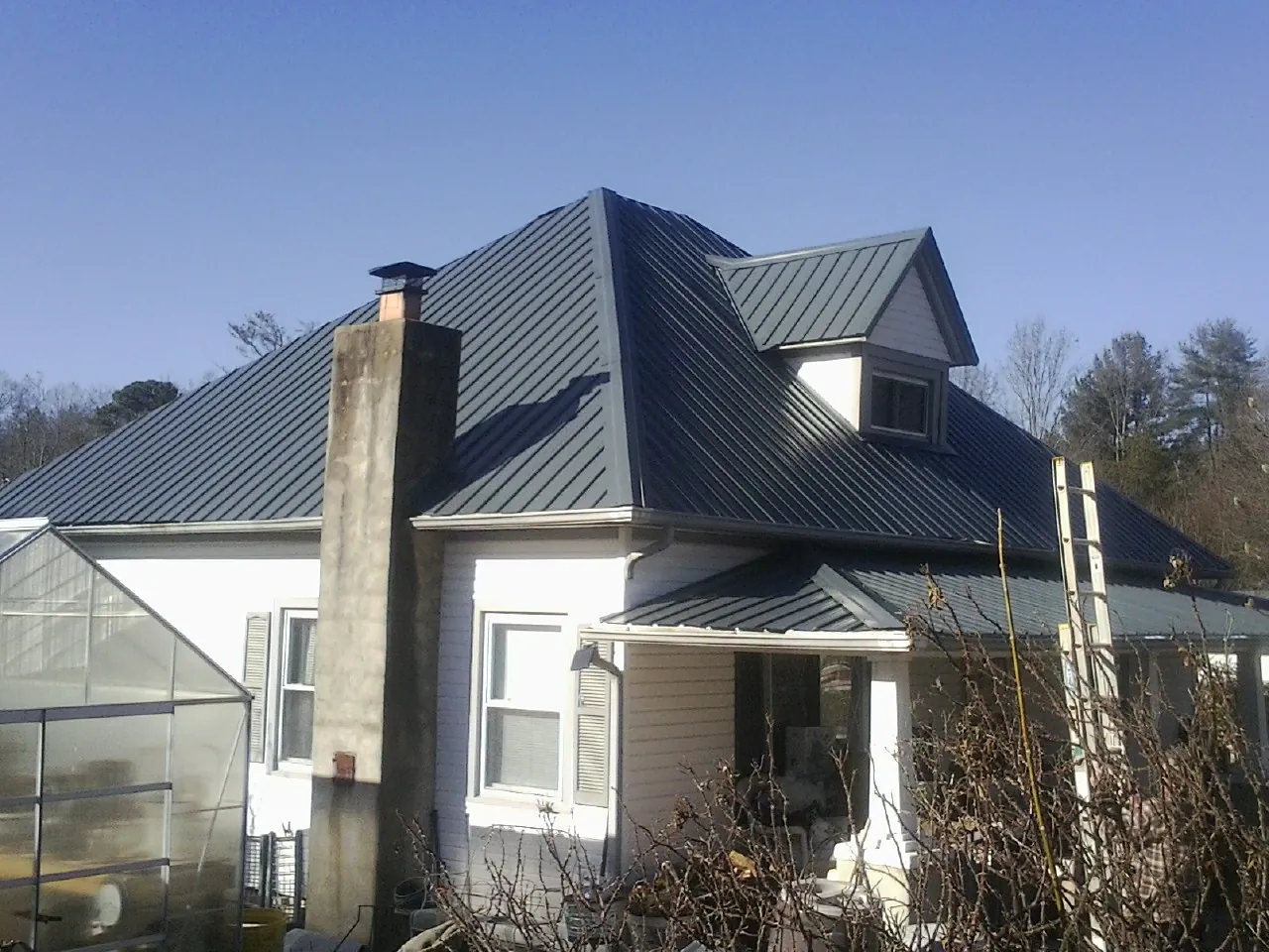 Dark blue standing seam metal roof on a white farmhouse with dormer — Slate & Tile Roof Repair by Roofing Brothers in Canastota
