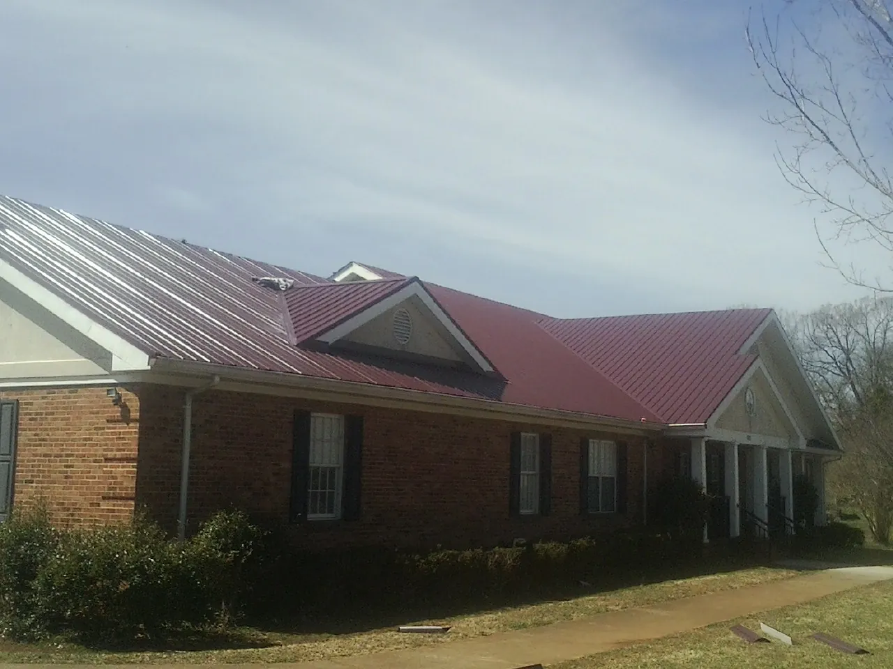 Red metal roof with gabled entries on a long brick building, from a Hail Damage Roof Repair job in Canastota