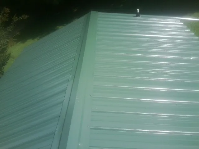 New green metal panels meeting at the ridge of a roof — Flat Roof Repair work by our crew in Canastota