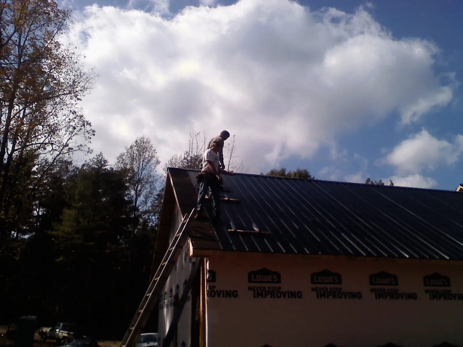 Roofer fastening dark metal panels high against a cloudy sky, from a Roof Inspection job in Canastota