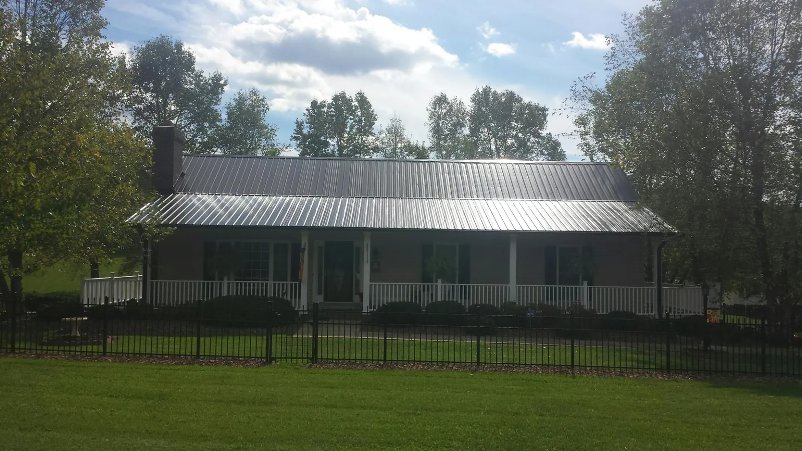 Gray metal roof on a brick ranch with a full width front porch — Gutter Guard Installation work by our crew in Canastota