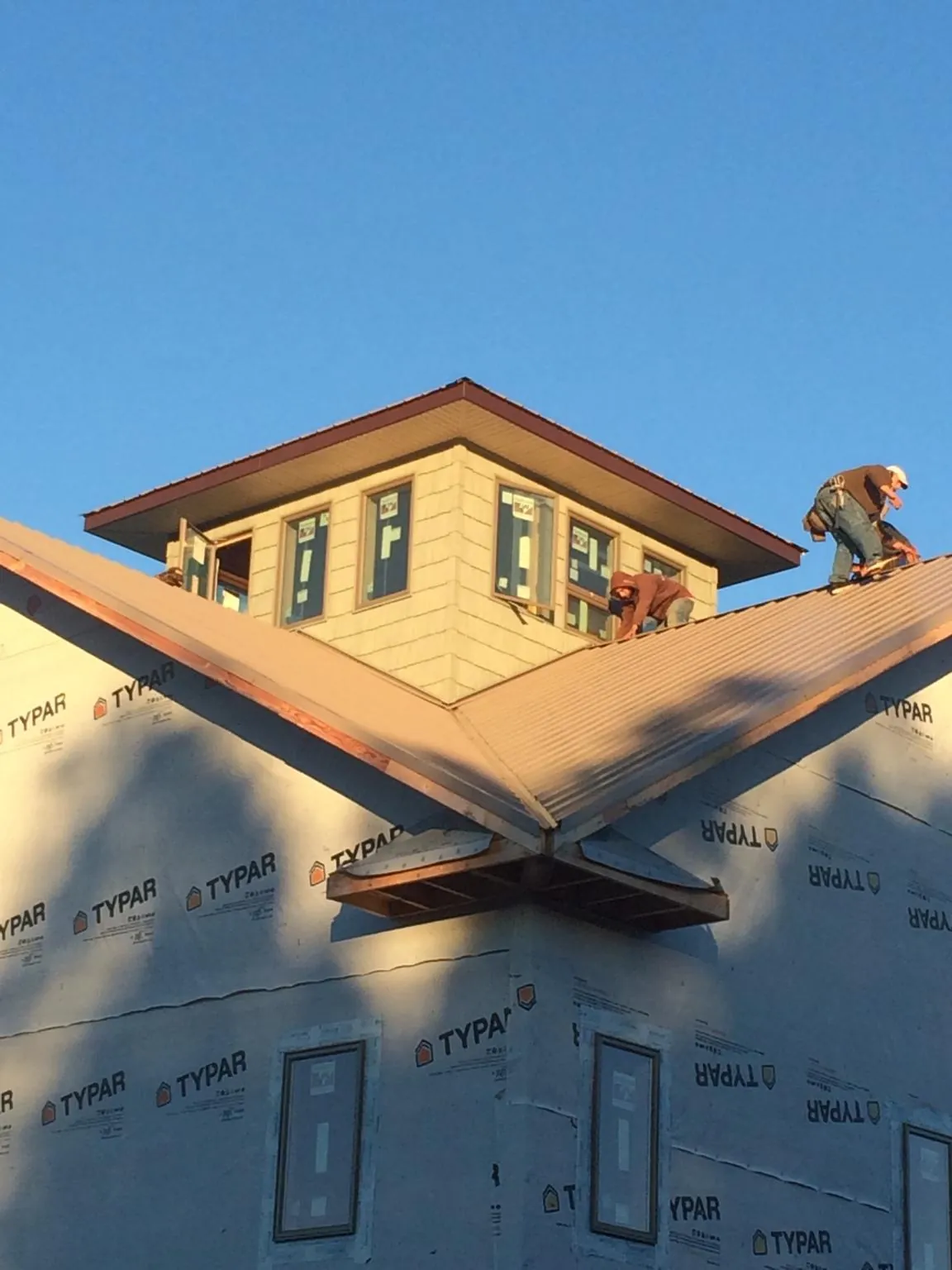 Roofers working around a rooftop cupola on a new metal roof at sunset — Roof Waterproofing in Canastota by Roofing Brothers